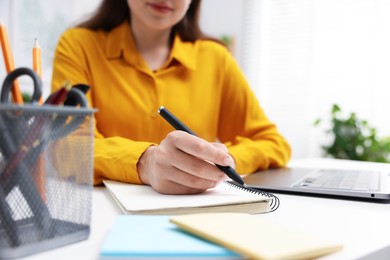 Photo of Woman with planner and laptop at white desk indoors, closeup