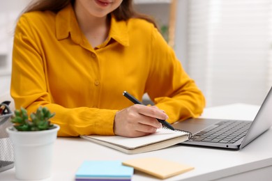 Photo of Woman with planner and laptop at white desk indoors, closeup