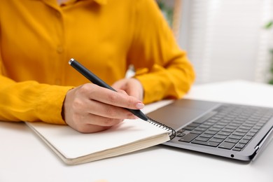 Photo of Woman with planner and laptop at white desk indoors, closeup