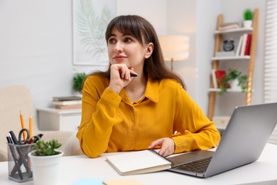 Photo of Woman with planner and laptop at white desk indoors