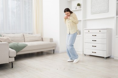 Photo of Emotional young woman looking in disgust at cockroaches on floor indoors. Pest problem