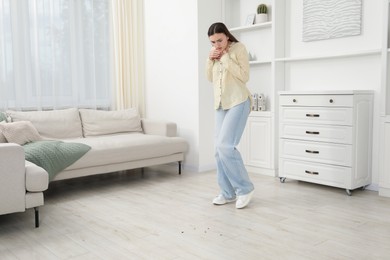 Photo of Emotional young woman looking in disgust at cockroaches on floor indoors. Pest problem
