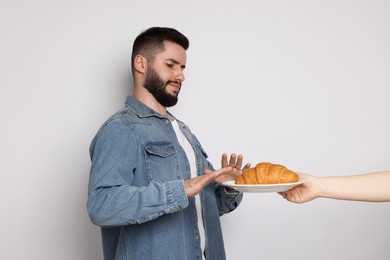 Photo of Gluten free diet. Man refusing from croissant on light grey background