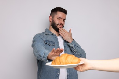 Photo of Gluten free diet. Man refusing from croissant on light grey background