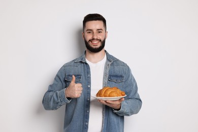 Photo of Gluten free diet. Man with croissant showing thumbs up on light grey background