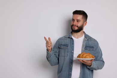 Photo of Gluten free diet. Man with croissant pointing at something on light grey background, space for text