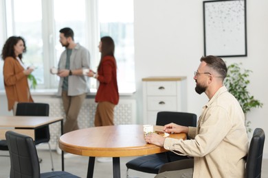 Photo of Man eating lunch at table. Colleagues having break in office