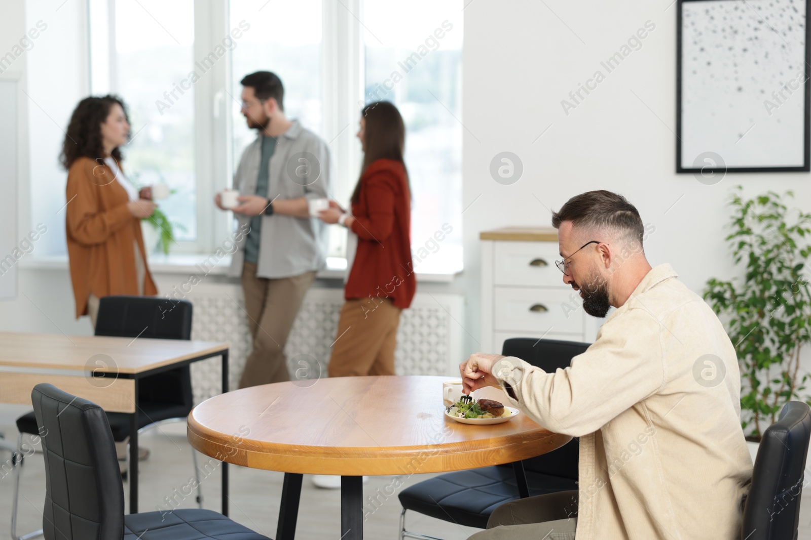 Man eating lunch at table. Colleagues having break in office Photo of Man eating lunch at table. Colleagues having break in office