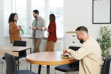 Photo of Man eating lunch at table. Colleagues having break in office