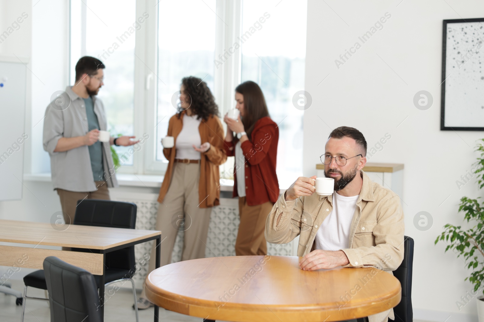 Man with coffee at table. Colleagues having lunch break in office Photo of Man with coffee at table. Colleagues having lunch break in office