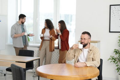 Photo of Man with coffee at table. Colleagues having lunch break in office
