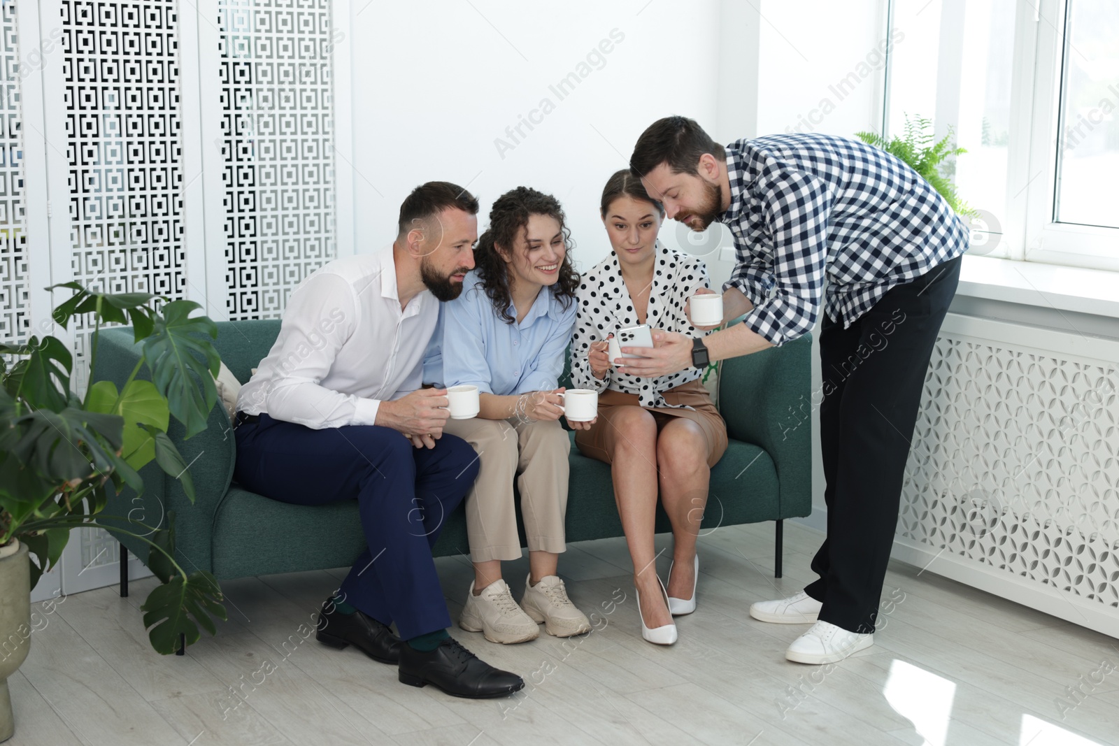Man showing colleagues something on his phone during coffee break in office Photo of Man showing colleagues something on his phone during coffee break in office