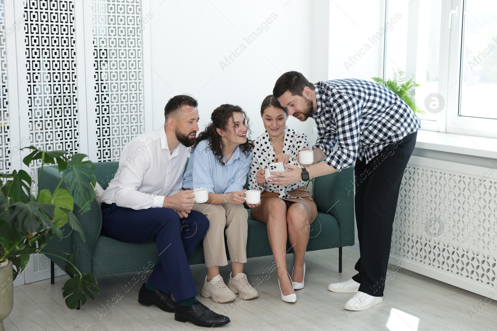 Man showing colleagues something on his phone during coffee break in office Photo of Man showing colleagues something on his phone during coffee break in office