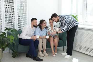 Photo of Man showing colleagues something on his phone during coffee break in office