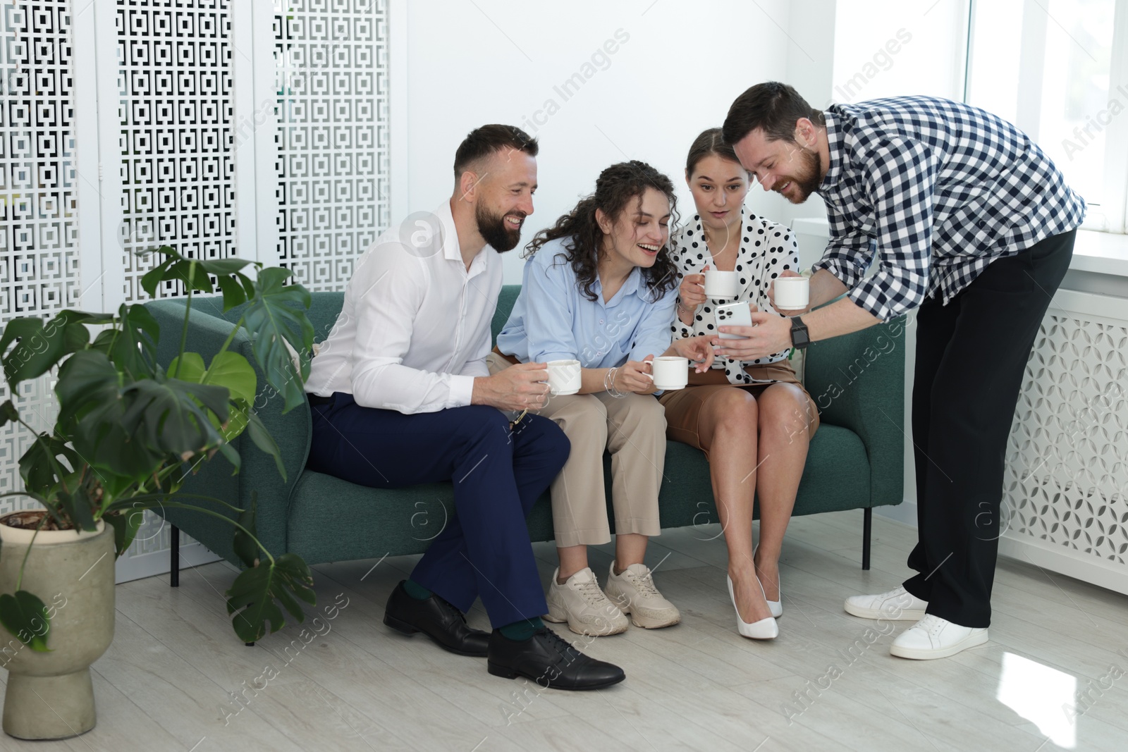 Man showing colleagues something on his phone during coffee break in office Photo of Man showing colleagues something on his phone during coffee break in office