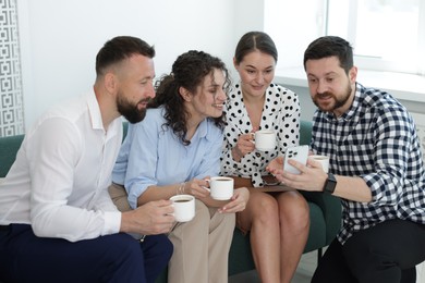 Photo of Man showing colleagues something on his phone during coffee break in office