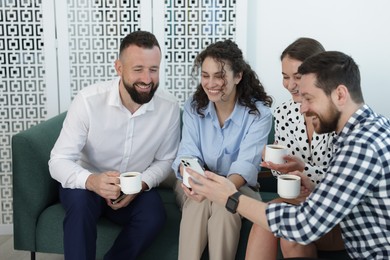 Photo of Man showing colleagues something on his phone during coffee break in office