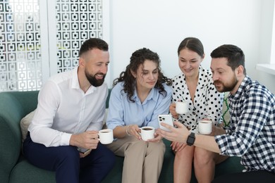 Photo of Man showing colleagues something on his phone during coffee break in office