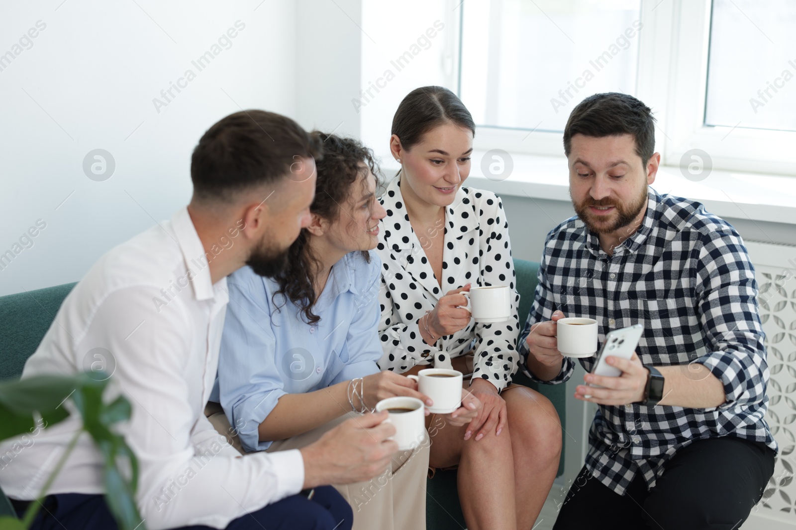 Man showing colleagues something on his phone during coffee break in office Photo of Man showing colleagues something on his phone during coffee break in office