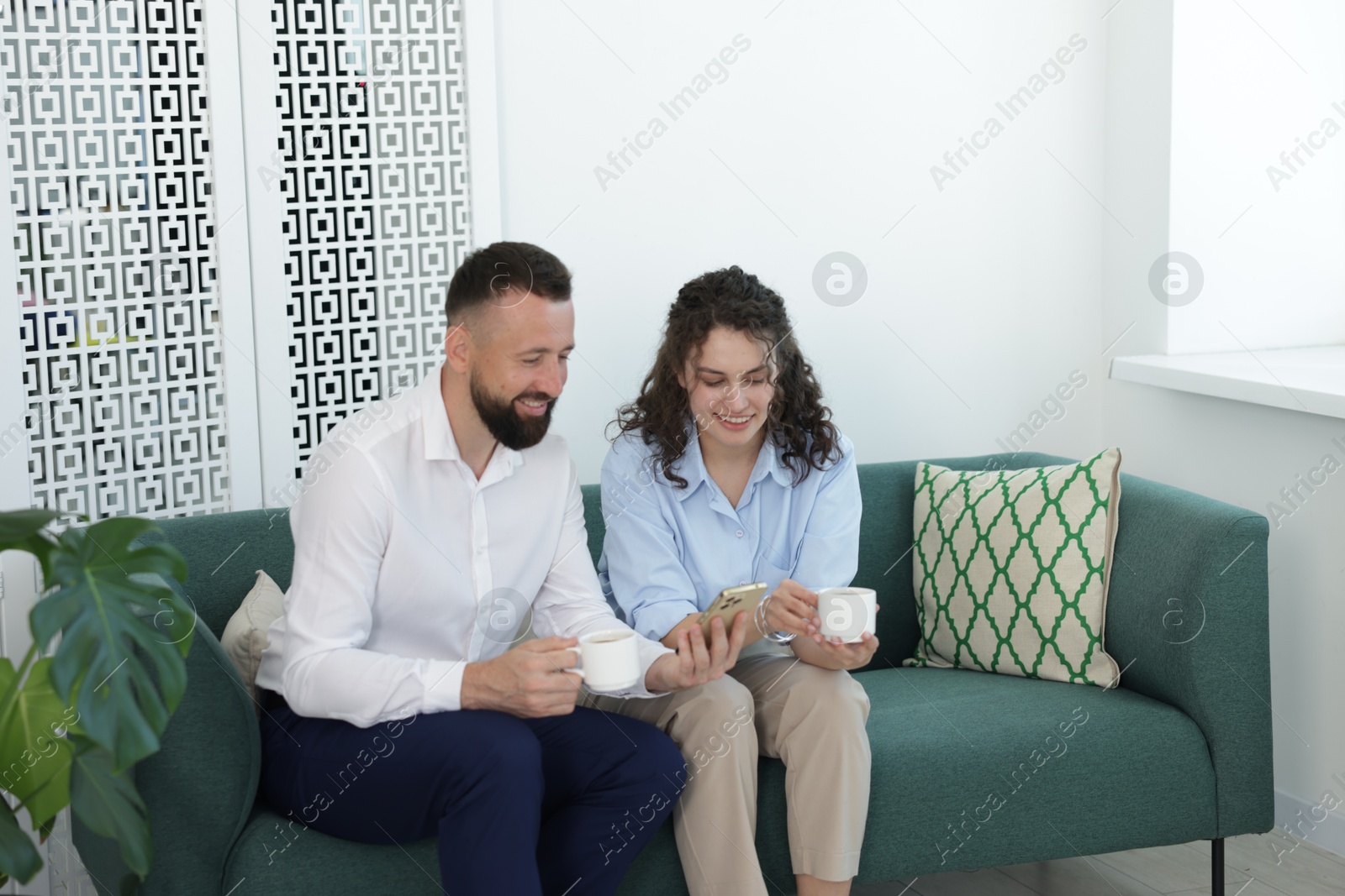 Man showing colleague something on his phone during coffee break in office Photo of Man showing colleague something on his phone during coffee break in office