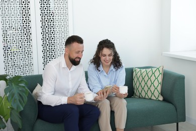 Photo of Man showing colleague something on his phone during coffee break in office