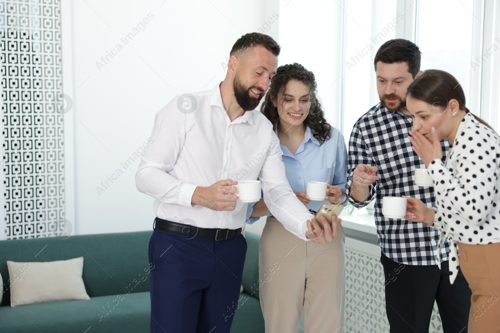 Man showing colleagues something on his phone during coffee break in office Photo of Man showing colleagues something on his phone during coffee break in office