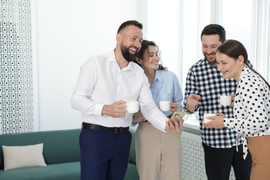 Photo of Man showing colleagues something on his phone during coffee break in office