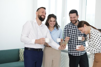 Photo of Man showing colleagues something on his phone during coffee break in office
