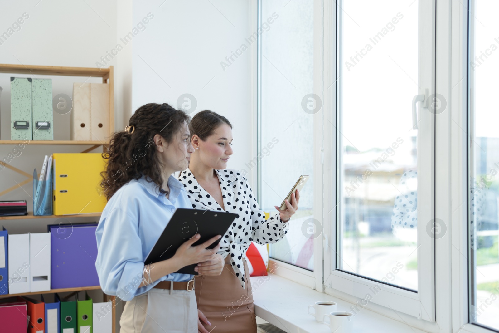 Colleagues looking out window during coffee break in office Photo of Colleagues looking out window during coffee break in office