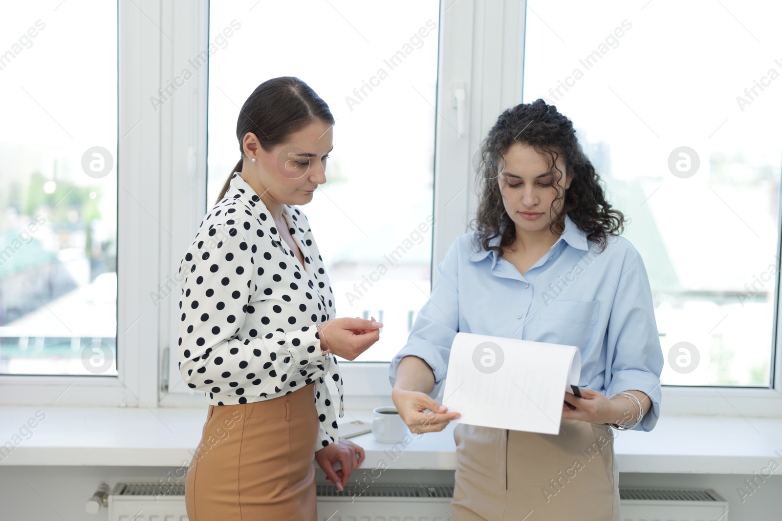 Colleagues discussing work near window in office Photo of Colleagues discussing work near window in office