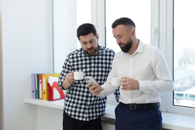 Photo of Colleagues with coffee and smartphone during lunch break in office