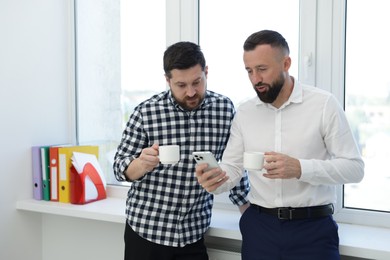 Photo of Colleagues with coffee and smartphone during lunch break in office