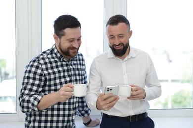 Photo of Colleagues with coffee and smartphone during lunch break in office