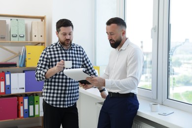 Photo of Colleagues with coffee and paperwork during lunch break in office