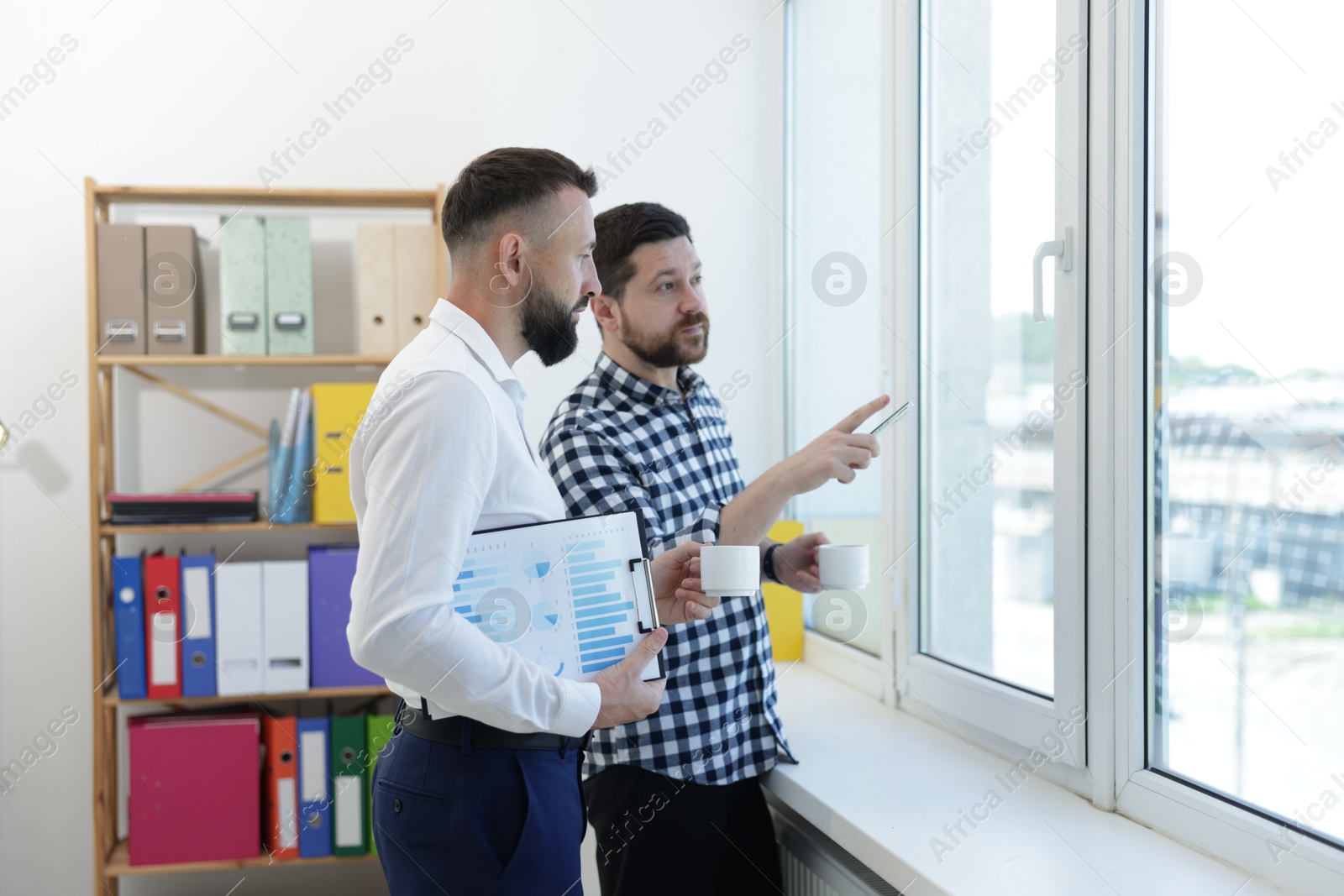 Colleagues looking out window during coffee break in office Photo of Colleagues looking out window during coffee break in office