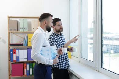 Photo of Colleagues looking out window during coffee break in office