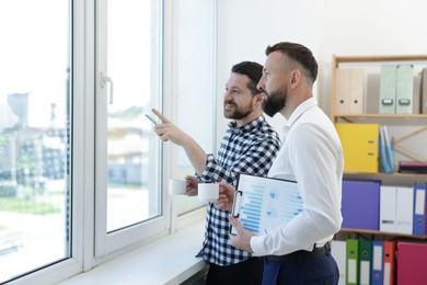 Photo of Colleagues looking out window during coffee break in office