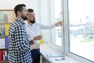 Photo of Colleagues looking out window during coffee break in office