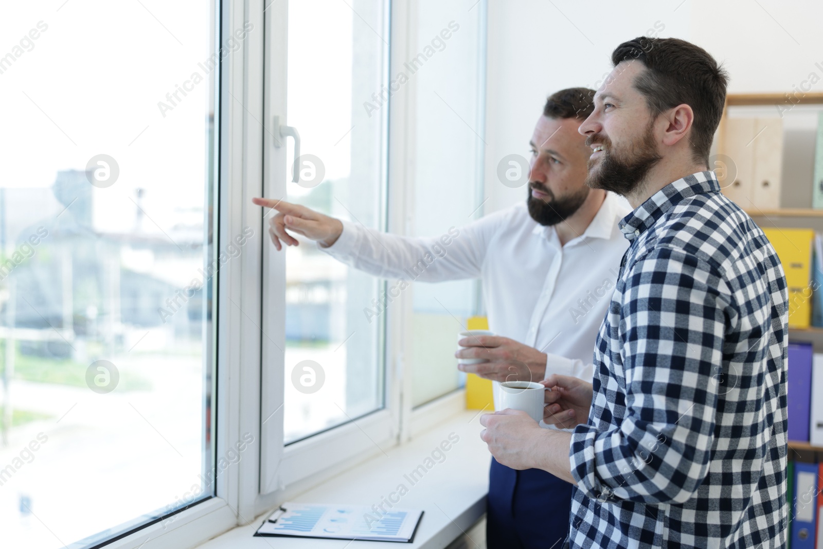 Colleagues looking out window during coffee break in office Photo of Colleagues looking out window during coffee break in office