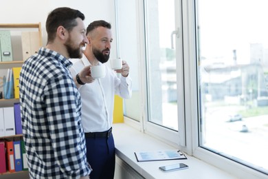 Photo of Colleagues looking out window during coffee break in office