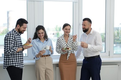 Photo of Colleagues with food and drinks near window in office during lunch break