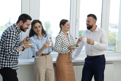 Photo of Colleagues with food and drinks near window in office during lunch break
