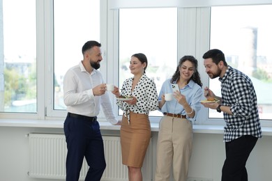 Photo of Colleagues with food and drinks near window in office during lunch break