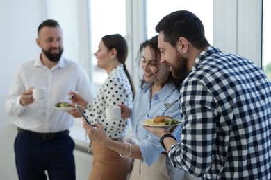 Photo of Colleagues with food and drinks near window in office during lunch break
