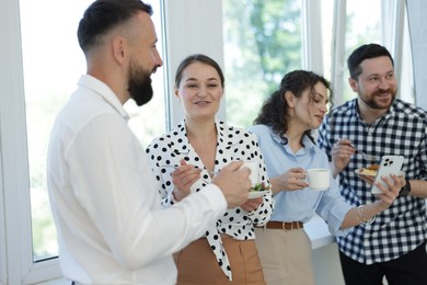Photo of Colleagues with food and drinks near window in office during lunch break
