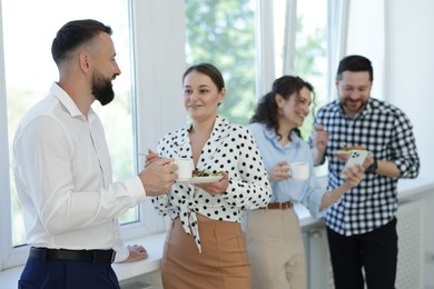 Photo of Colleagues with food and drinks near window in office during lunch break