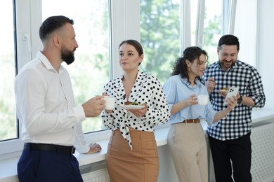 Photo of Colleagues with food and drinks near window in office during lunch break