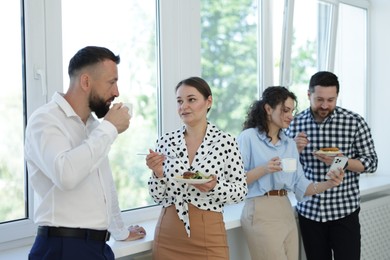 Photo of Colleagues with food and drinks near window in office during lunch break