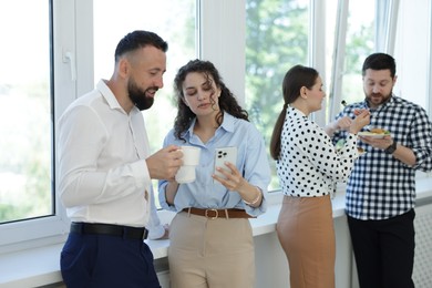 Photo of Colleagues with food and drinks near window in office during lunch break