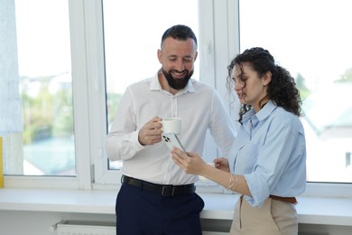 Photo of Colleagues with coffee and smartphone near window in office during lunch break